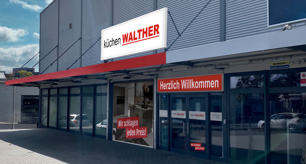 Eingang Küchenstudio mit Willkommen-Schild und Werbebannern "Wir schlagen jeden Preis"