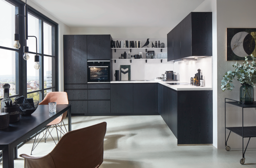 Nobilia L-Küche mit grifflosen Fronten in schwarzer Eichenstruktur, weißer Mineralstein-Arbeitsplatte und wandmontierten Stahlregalen – urbanes Küchendesign mit Stadtblick, cognacfarbenen Lederstühlen und Edison-Pendelleuchten